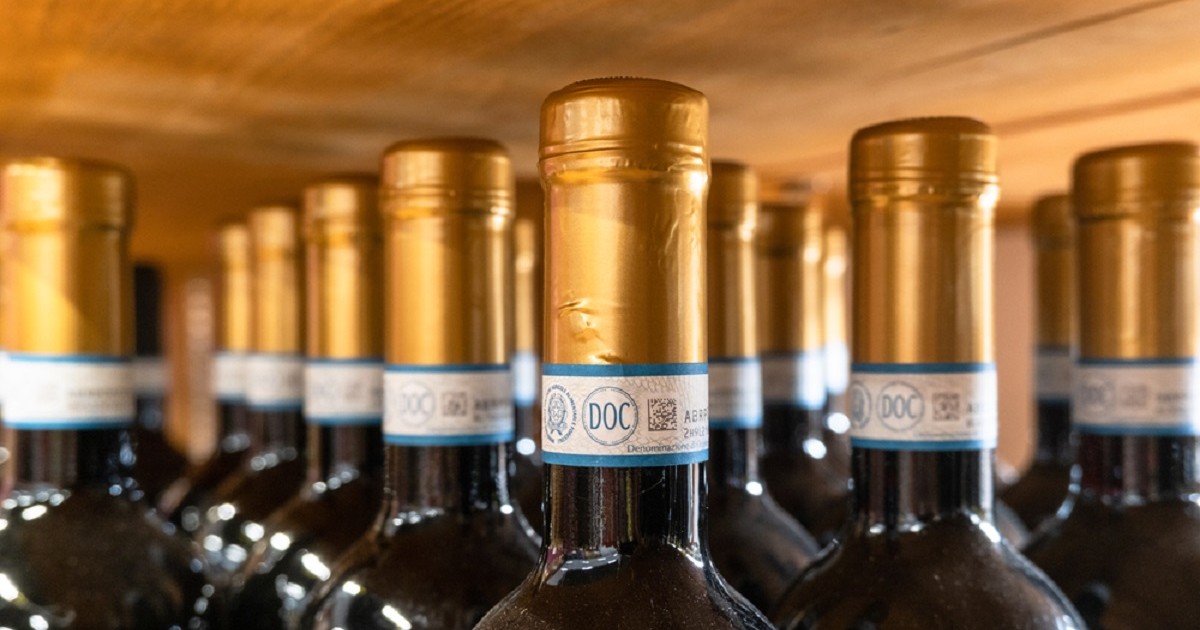 Care este diferenţa între denumirile de origine DOC, DOCG şi DOP - Imagine cu sticle de vin roşu italian, in care sunt scoase în evidenţă etichetele de pe gâtul sticlelor pe care este trecută indicaţia geografică DOC