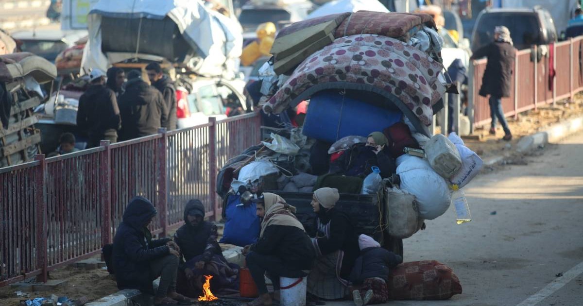 palestinieni pe marginea drumului cu un foc facut in mijlocul lor langa ei au saltea de pat si multe obiecte din case