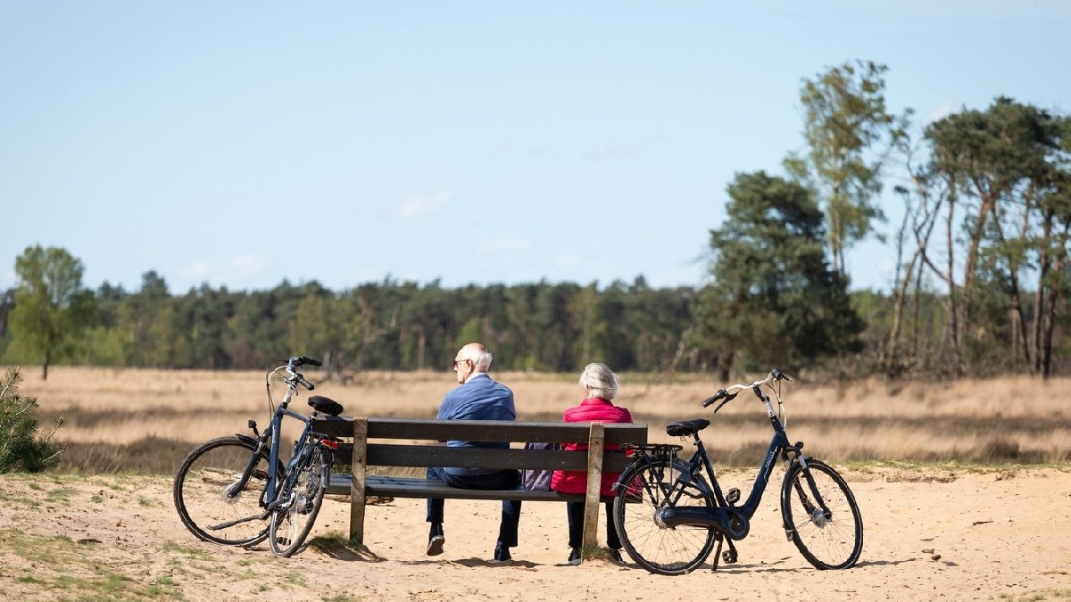 Un cuplu de pensionari cu biciclete se odihnește pe o bancă în rezervația naturală „Strabrechtse Heide” din Țările de Jos