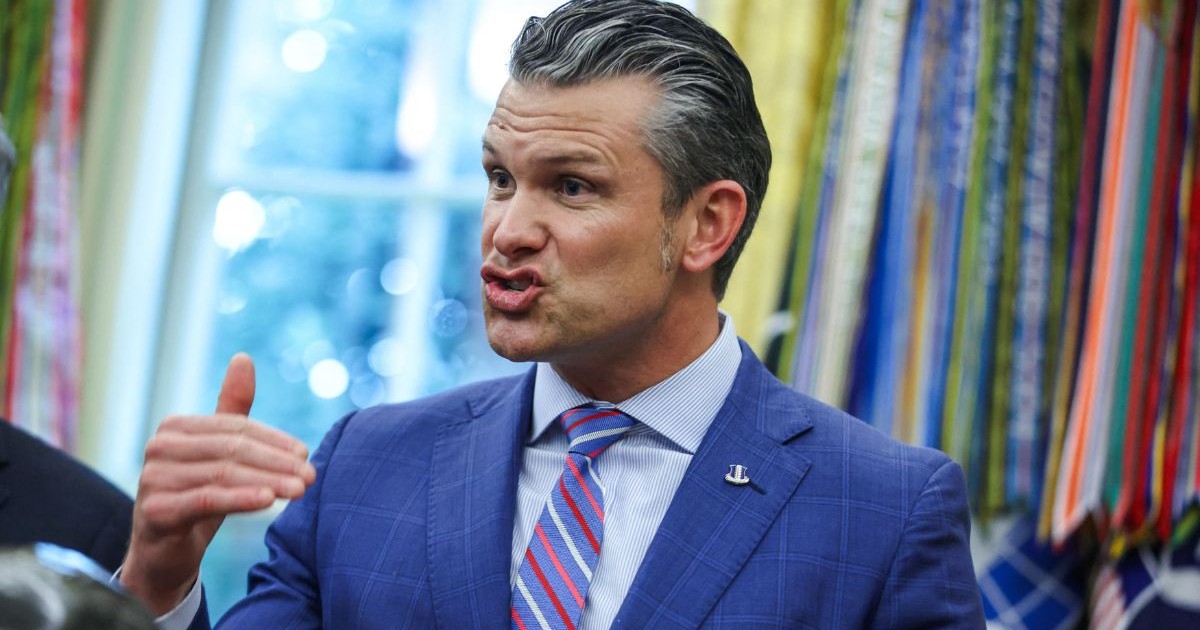 Pete Hegseth, îmbrăcat într-un sacou albastru, o cămașă bleu și o cravată mov cu dungi gesticulând cu mâinile și făcând o grimasă în timp ce vorbește, în biroul oval din SUA, Washington DC, Septembrie 2025