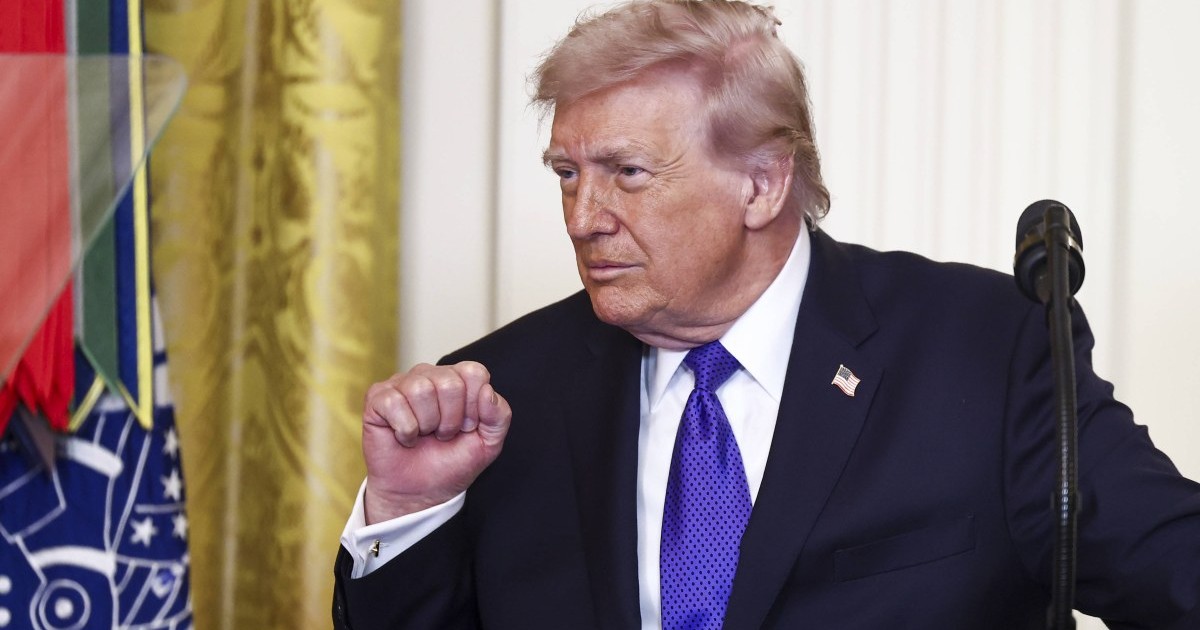 Donald Trump de la bust în sus, stând în spatele unui podium de culoare închisă pe un fundal de un alb mat cu detalii de panouri verticale. El privește spre stânga cadrului cu o expresie serioasă, având părul blond-roșiatic și mâna dreaptă ridicată în dreptul pieptului cu pumnul strâns. Este îmbrăcat într-un sacou negru, cămășă albă și o cravată de un violet aprins cu un model discret, având pe reverul stâng o mică insignă cu steagul Statelor Unite