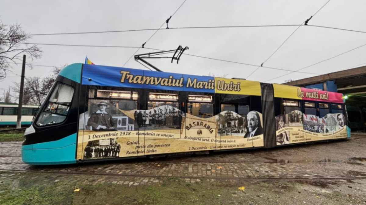 Un tramvai acoperit cu un colaj grafic istoric pe care scrie „Tramvaiul Marii Uniri”. Acesta se află într-un depou, pe o vreme mohorâtă.