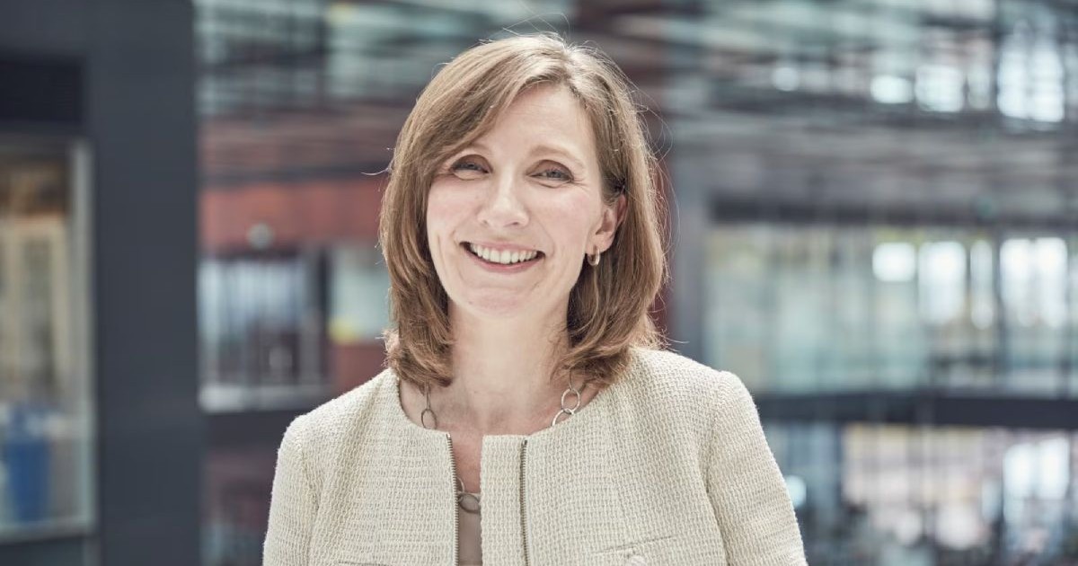 Moira Gilchrist de la PMI, îmbrăcată în bej, în fața unei clădiri cu fațadă de sticlă.