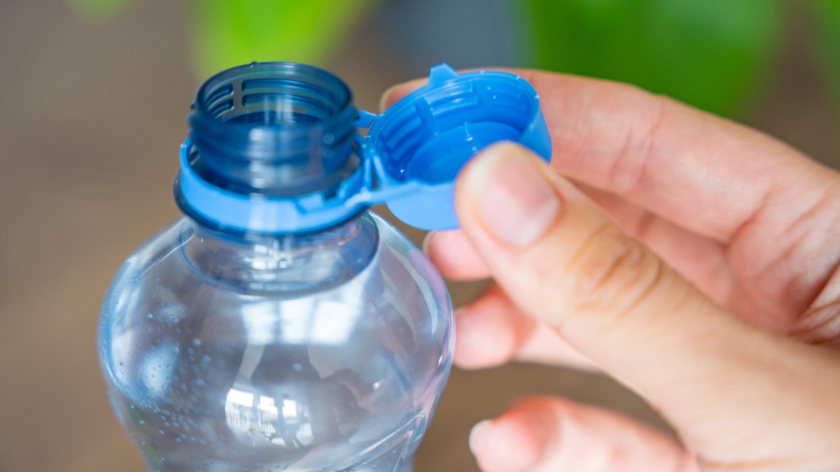 O persoană care ține o sticlă de plastic în mână, cu dopul desfăcut.