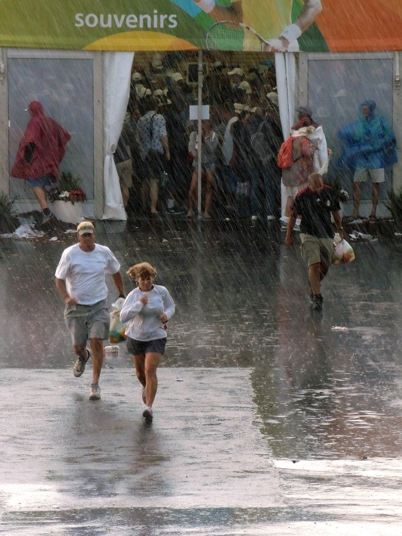 epa04682819 Tennis patrons crowd in the souvenirs tent (behind) and run to get out of the rain during a rain delay at the Miami Open tennis tournament on Key Biscayne, Miami, Florida, USA, 27 March 2015. EPA/RHONA WISE
