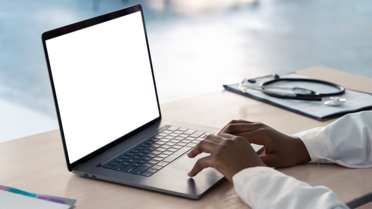 Un doctor care se află la birou și folosește un laptop care are ecranul alb