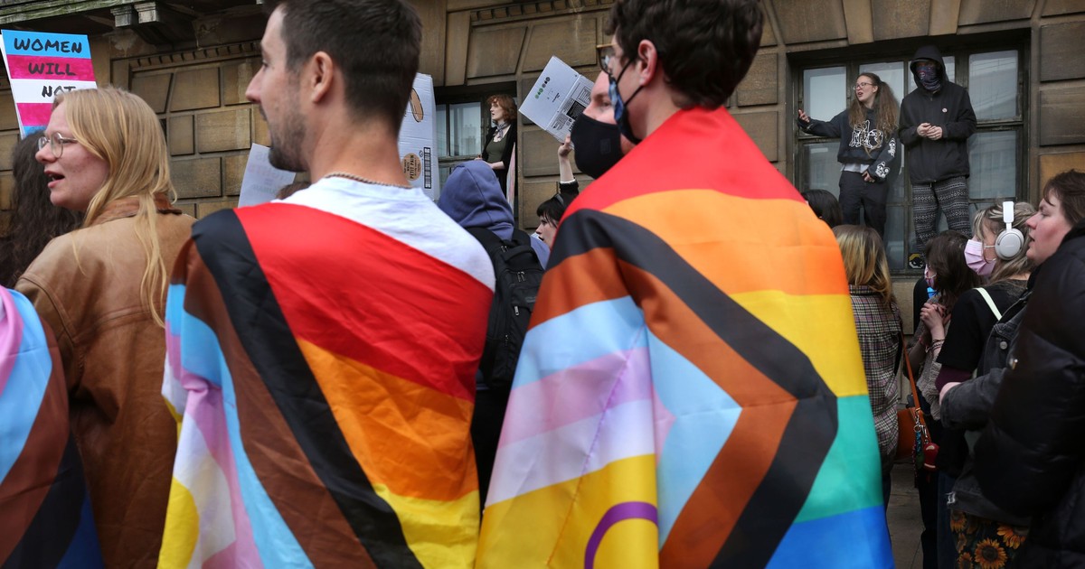 Protestatarii înfășurați în steaguri trans ascultă discursurile ținute în fața Crții Supreme, în timp ce alții se urcă pe pervazele clădirii în timpul protestului
