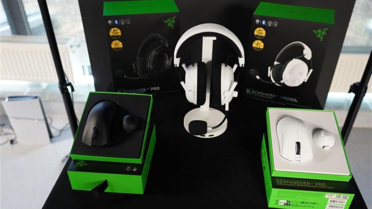 Căștile Razer Blackshark V3 Pro albe pe un stand de expozițe, încadrade de doi mouși Razer, unul negru și unul alb.
