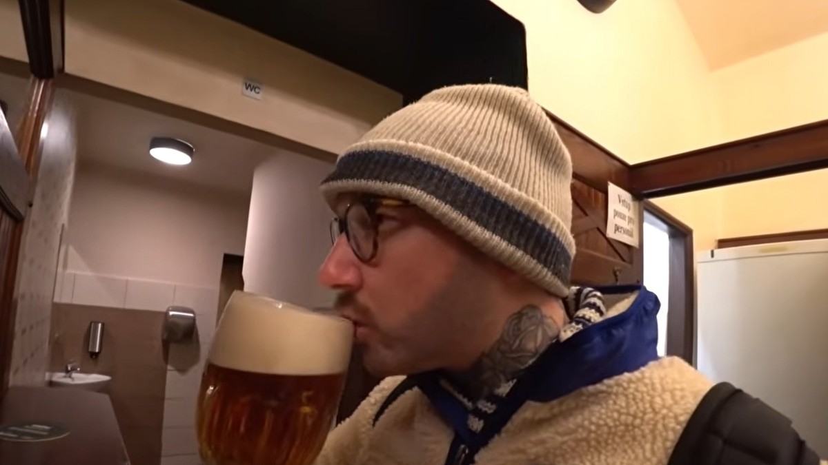 Un bărbat cu o căciulă albă și o geacă albă, într-un bar din Cehia, în timp ce bea bere dinrtr-o halbă