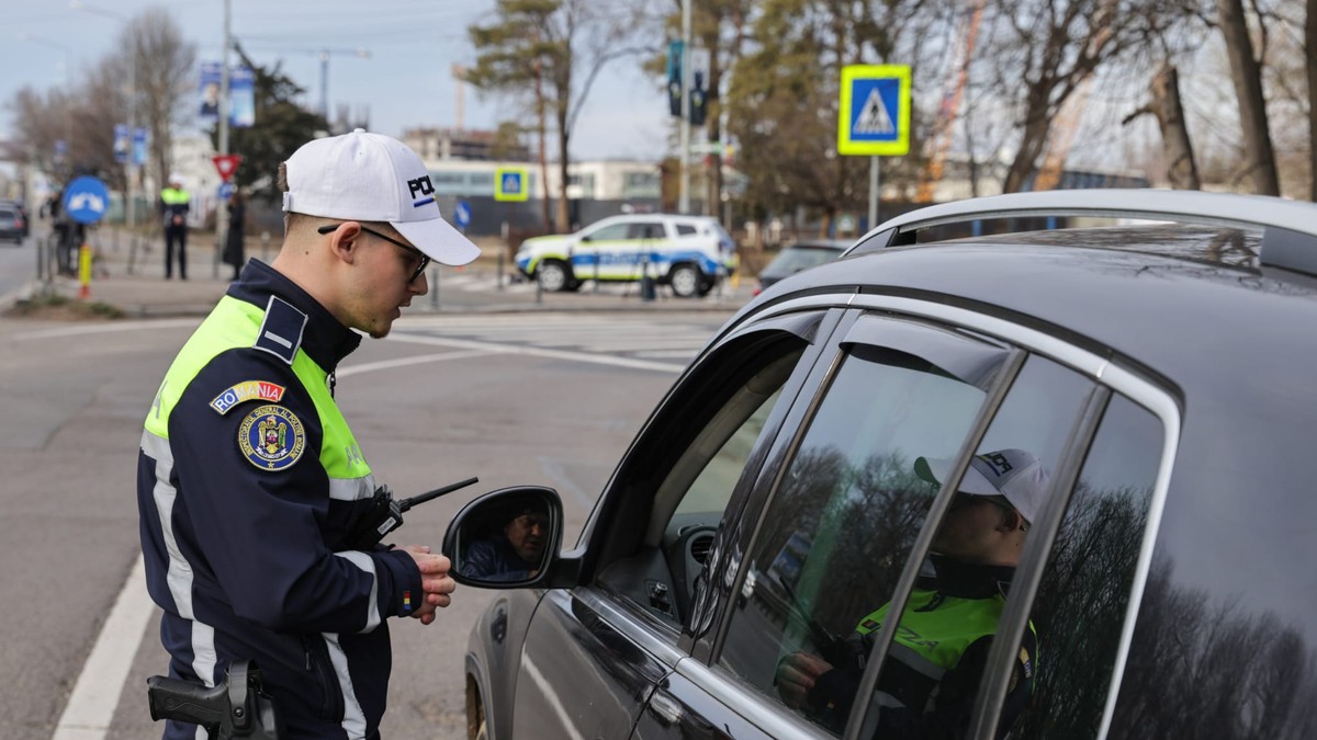 Un polițist rutier lângă o mașină neagră care are geamul deschis