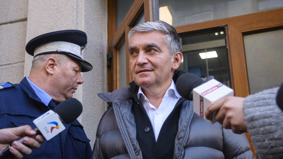 Vlad Oprea surprins în timp ce pleacă de la sediul DNA, pe 28 ianuarie 2024. În stânga e un polițist, iar primarul din Sinaia are în față două microfoane
