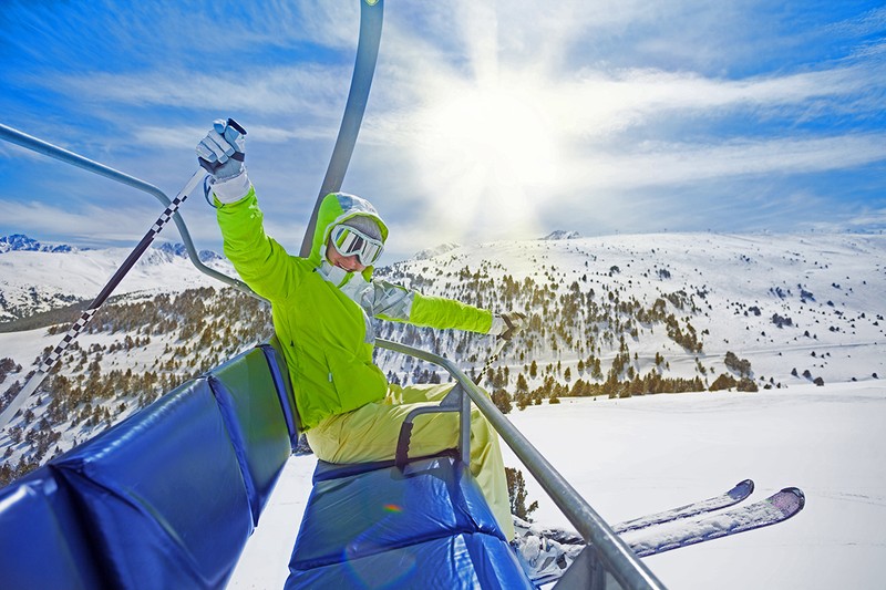21002279 - happy young woman skier sitting on ski lift chair, smiling and happily lifting her hands