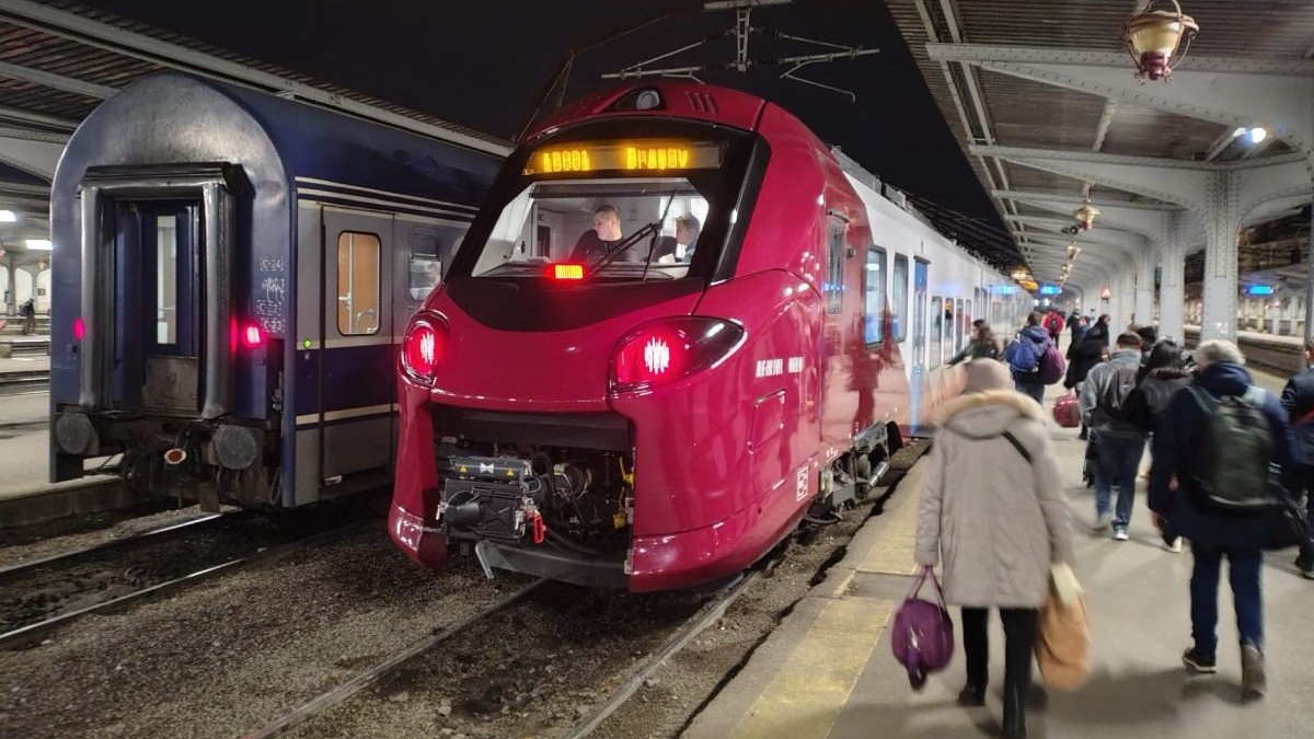 Tren al CFR Călători, de culoare roșie, în gara CFR din București, în timp ce mai mulți oameni se află pe peron