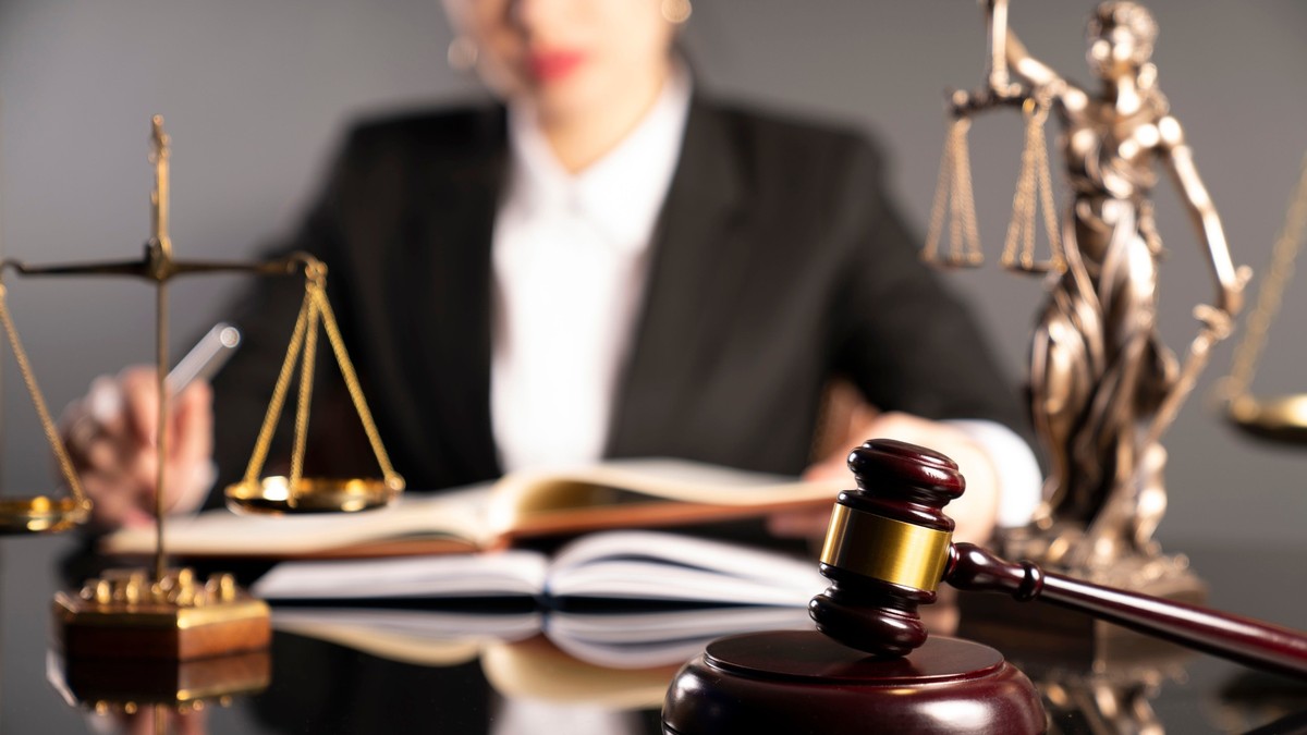 Ce face un notar – lista notarilor din București - Imagine cu mai multe obiecte de pe biroul unui notar, o balanţă, o statuie a zeiţei Themis şi un ciocănel de justiţie, aflate pe un birou, în faţa unei femei