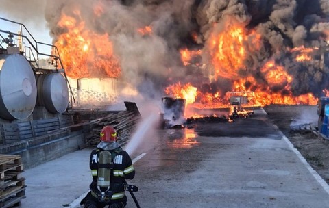 În curtea unei hale industriale, un pompier echipant cu aparat de respirat stă în genunchi pe o platformă betonată și direcționează un jet de apă spre un incendiu violent, sutești, valcea, 3 octombrie 2026