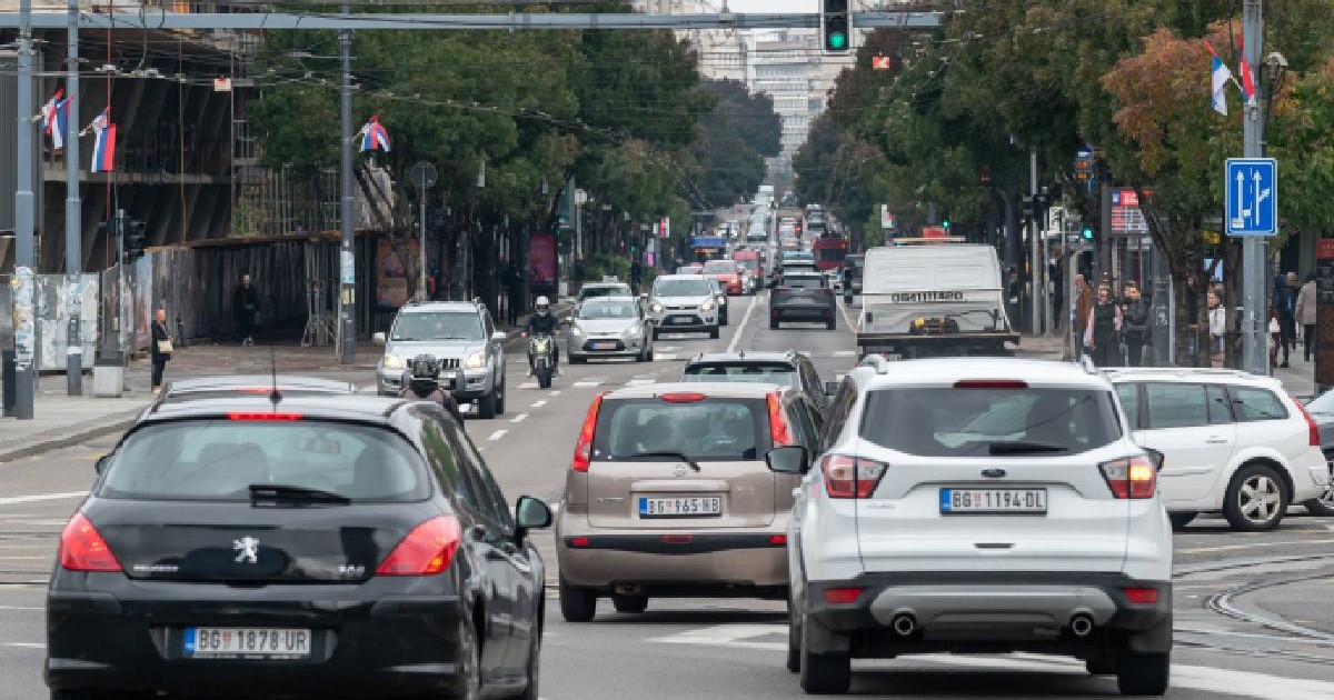 Imaginea arată o șosea urbană pe care circulă mai multe vehicule, inclusiv un camion și motociclete.