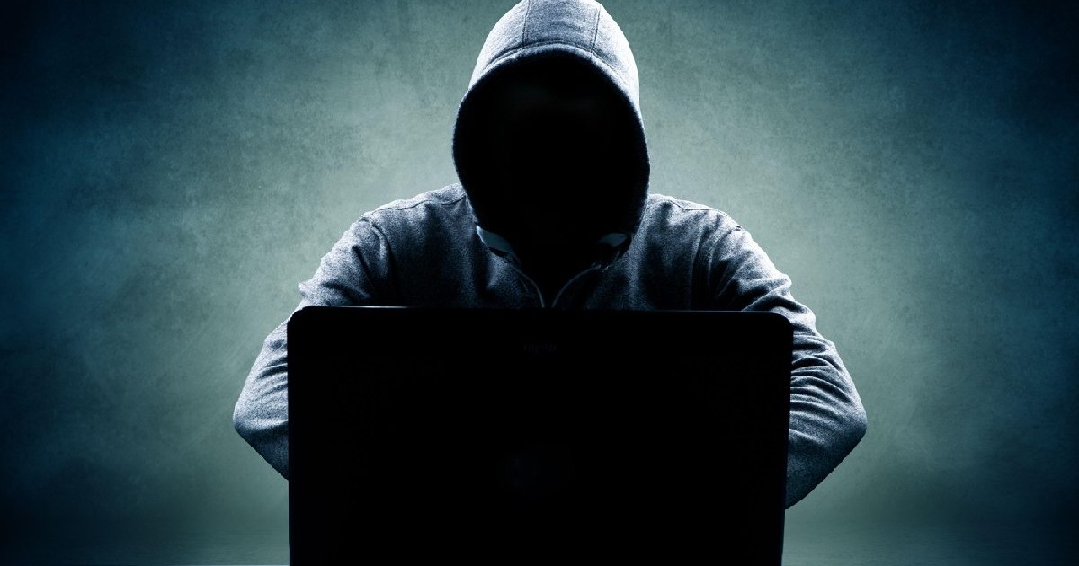 Bărbat în hanorac, cu fața ascunsă, stând în fața unui laptop