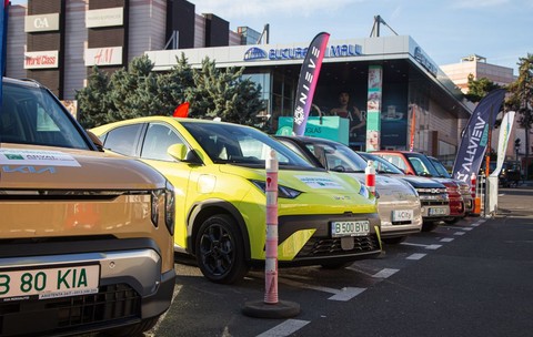 masini insirate in parcare cu steaguri de reclama in spatele unui mall
