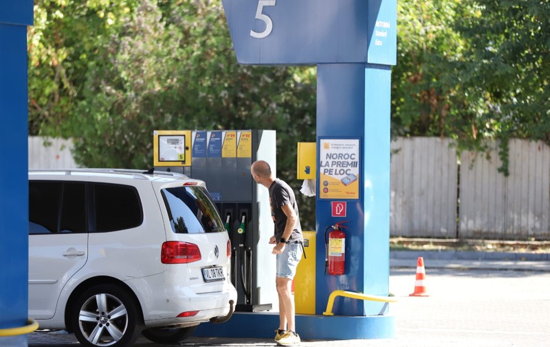 Un bărbat care se uită la ecranul unei pompe dintr-o stație de carburanți, lângă un autoturism alb Volkswagen parcat pentru alimentare.