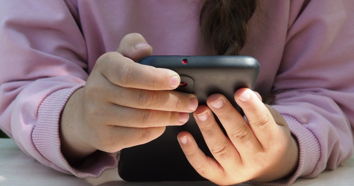 O fetiță care stă așezată și folosește un telefon.