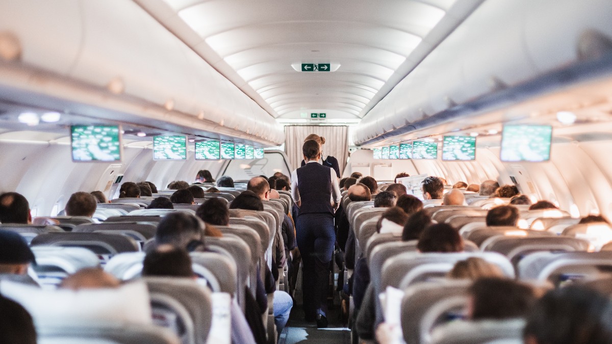 Interiorul unui avion cu pasageri așezați pe scaune și însoțitoarele de zbor pe culoarul aeronavei