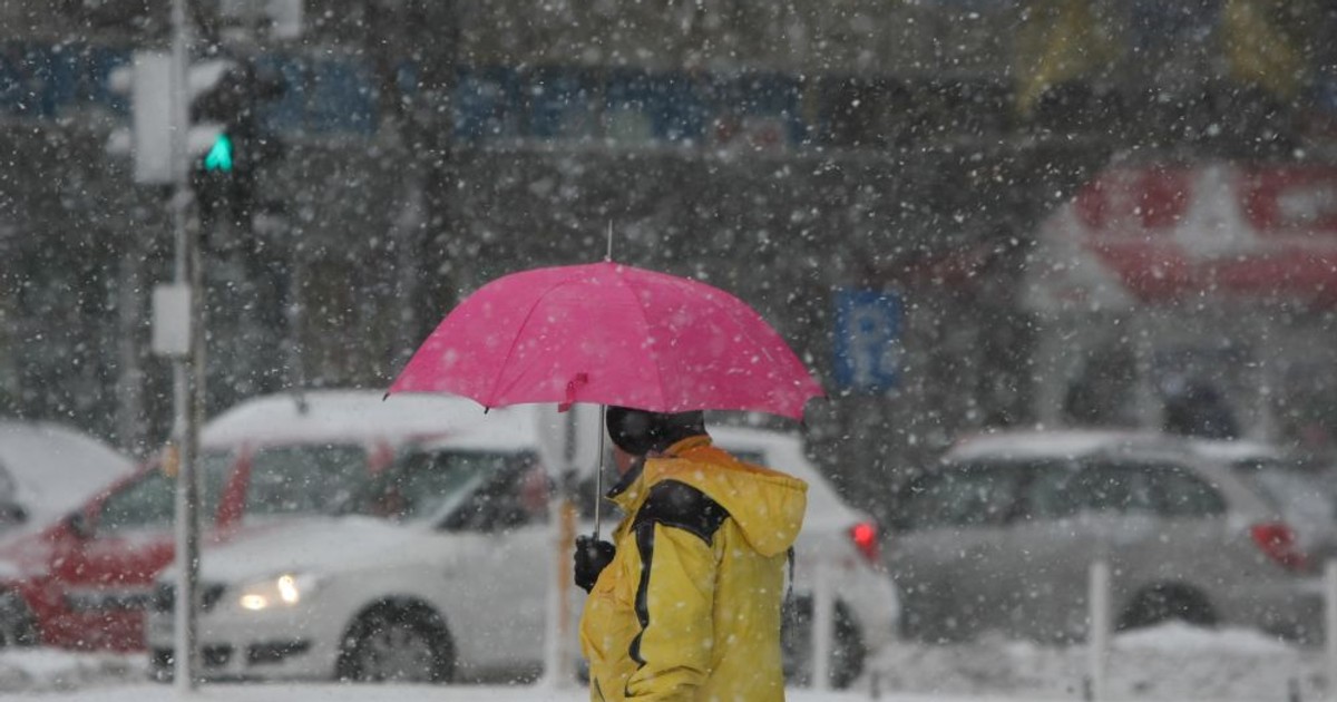 Vremea în București, pe 29 ianuarie. Un bărbat cu geacă galbenă ține o umbrelă roz, în plină ninsoare