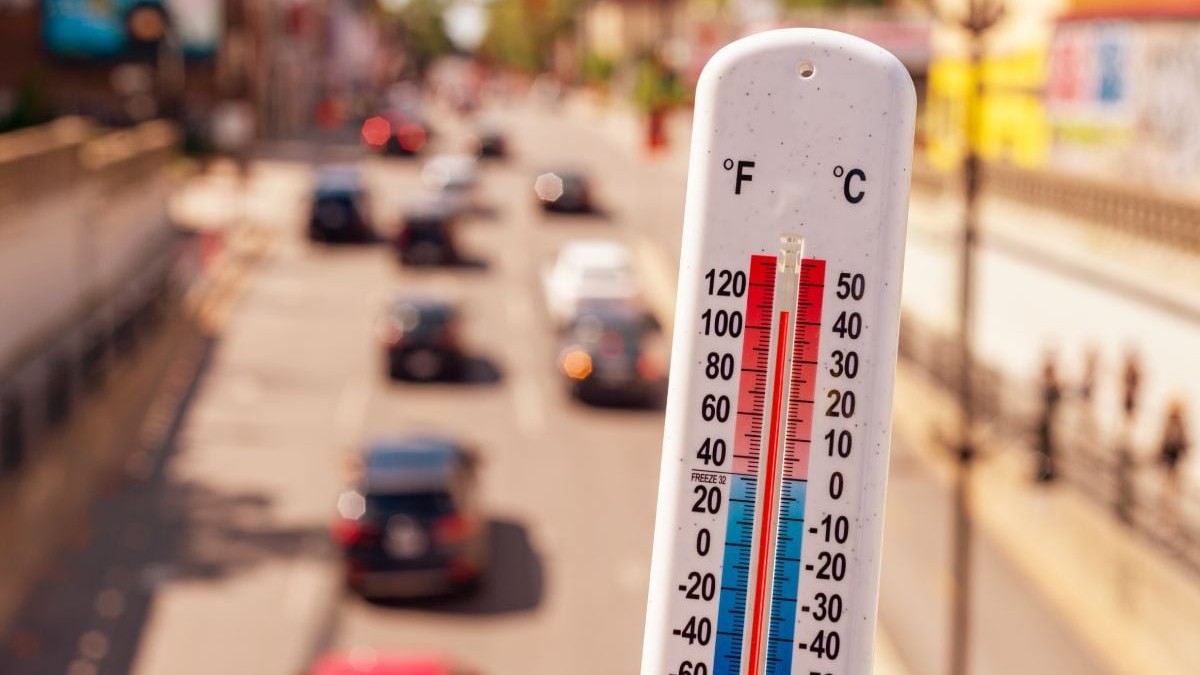 Termometru alb care indică o temperatură de 40 de grade Celsius, iar pe fundal, în blur, mașini care circulă pe o stradă
