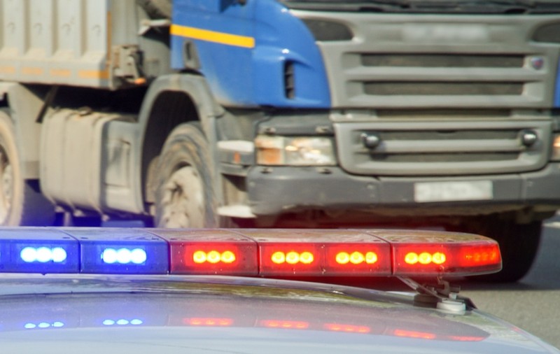 Rampa cu girofaruri roșii și albastre a unei mașini de poliție în prim-plan, având în fundal un camion oprit pe drum.