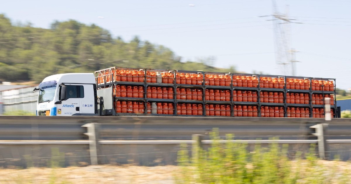 Camion alb transportând numeroase butelii de gaz portocalii pe autostradă