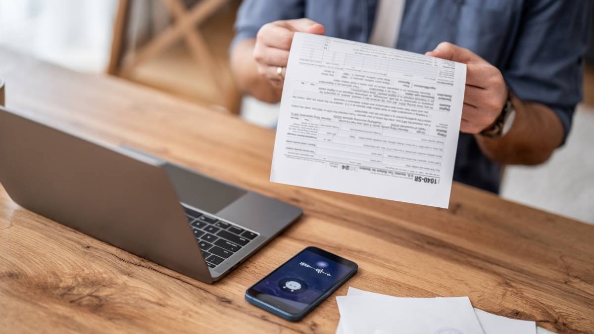 Bărbat care completează formulare fiscale folosind laptopul și smartphone-ul