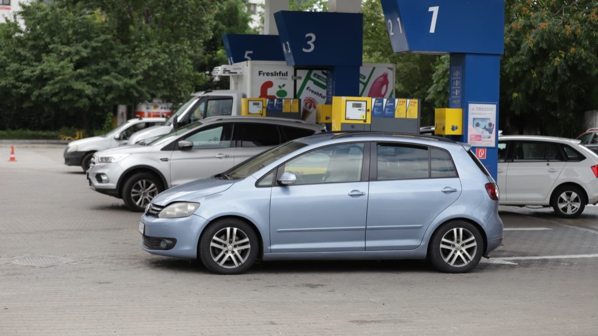 Mai multe mașini parcate la pompele numerotate ale unei stații de carburanți, având în prim-plan un autoturism Volkswagen Golf