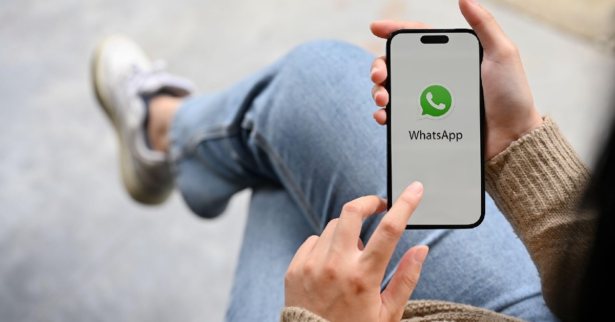 O mână de femeie ținând un smartphone cu logo-ul aplicației WhatsApp pe ecran.
