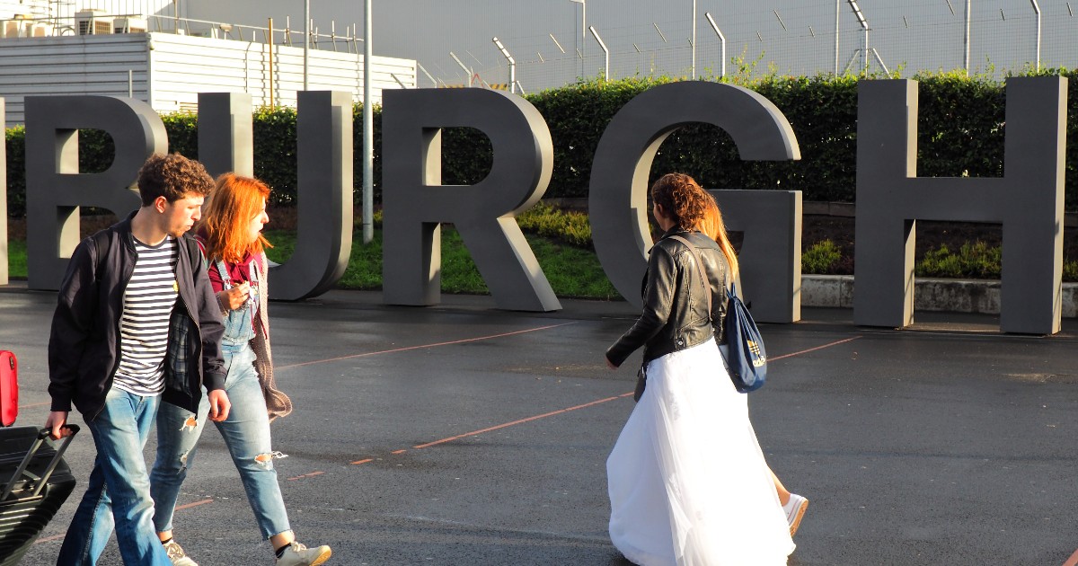 O mireasă roșcată cu o rochie albă, peste care are o geacă de piele, în aeroport, în timp ce pleacă în vacanță