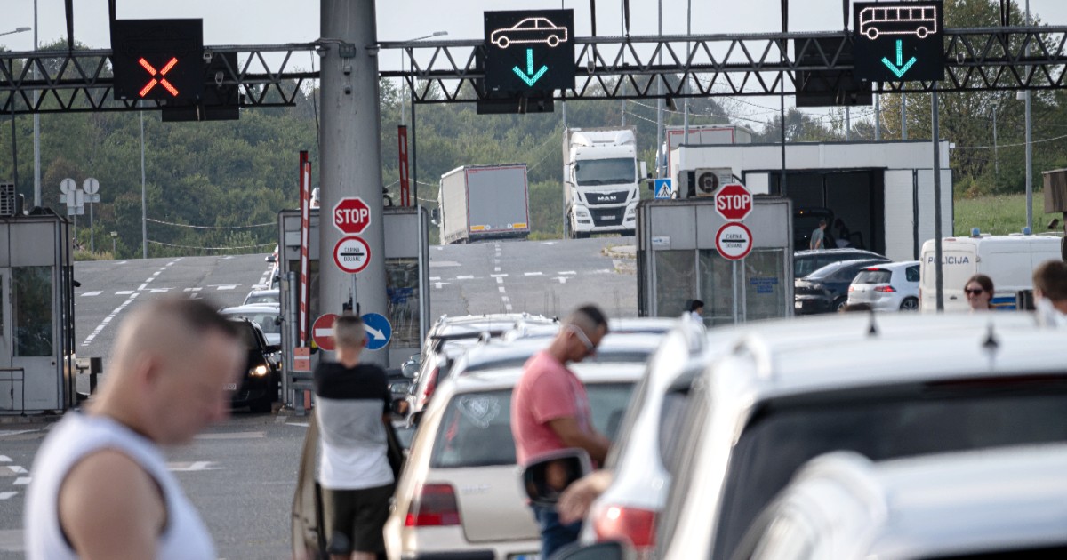 Un punct de control la frontieră aglomerat, unde mai multe autoturisme și persoane așteaptă la coadă în fața cabinellor vamale.