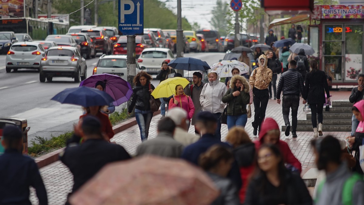 Un grup de oameni care merg pe stradă într-o zi ploioasă, au umbrelele desfăcute