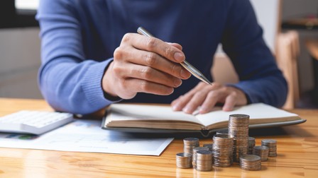 saving concept the male who is holding a silver pencil counting his money and doing revenue account on his notebook.