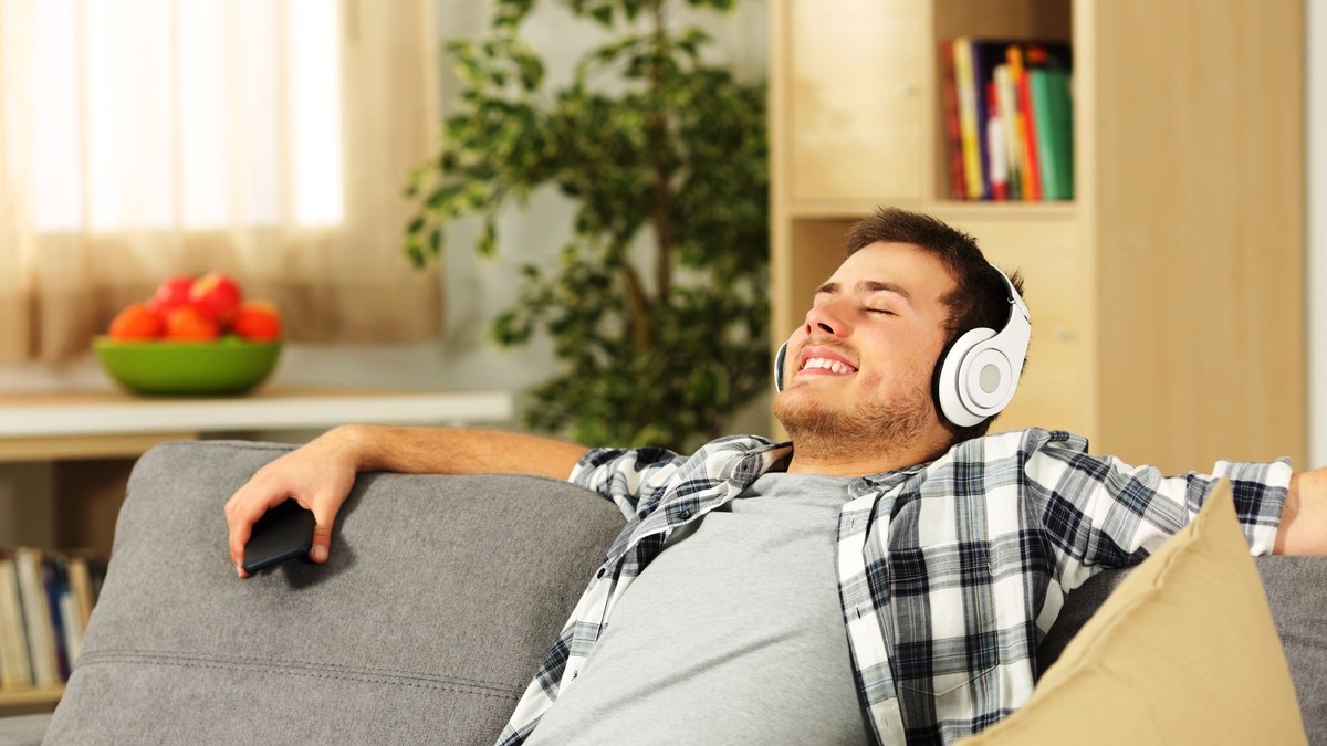 Curatare casti mobile- Un tanar sta relaxat pe canapea si asculta muzica