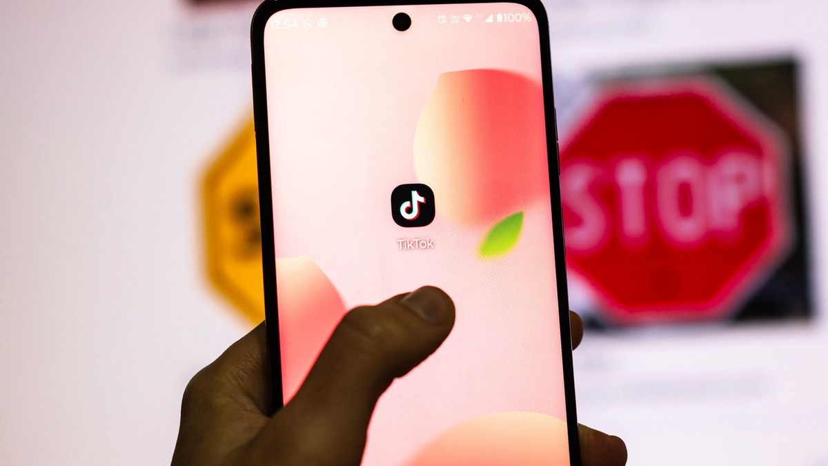 logo tiktok afisat pe telefon, cu un semn de circulație de stop afișat pe un ecran în fundal, blurat