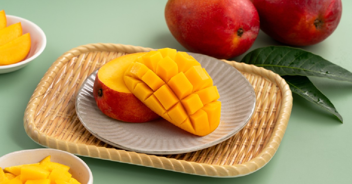 Cuburi suculente de mango galben cu mango întreg pe un fundal de masă verde.