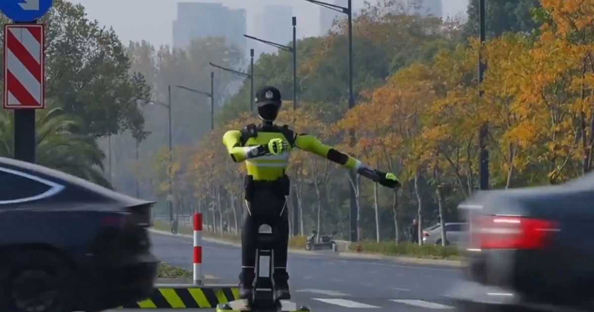 Un robot umanoid negru cu vestă verde neon care stă în mijlocul unei intersecții și dirijează traficul