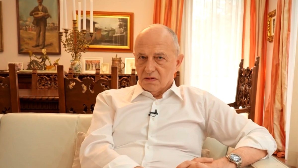 Mircea Geoană, îmbrăcat cu o cămașă albă, pe canapeaua din livingul casei sale