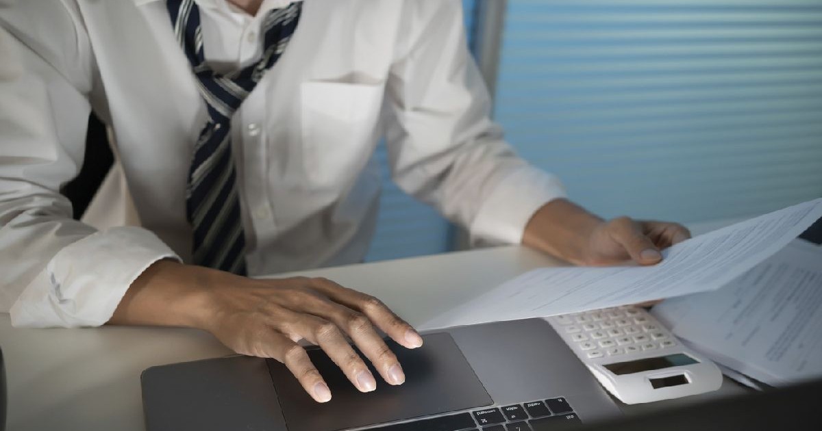Bărbat în cămașă albă și cravată neagră cu dungi albe lucrează la laptop în biro