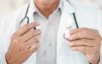 Un doctor îmbrăcat în halat alb, purtând un stetoscop în jurul gâtului, care ține o seringă cu ac și un flacon mic de sticlă