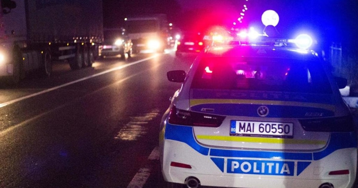 O mașină de poliție, cu girofarurile aprinse, este staționată pe partea dreapta, noaptea