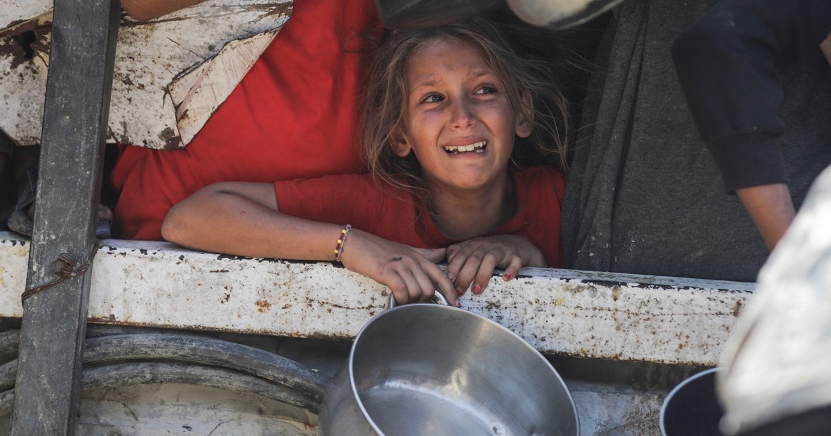 Imagine cu o fetiță care ține într-o mână o oală goală, în Gaza. Foto din 25 iulie 2025. Poartă o bluză roșie