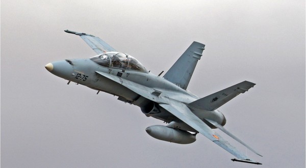 Un avion de luptă F/A-18 Hornet surprins în zbor în timp ce efectuează o manevră de urcare pe un cer înnorat.   
