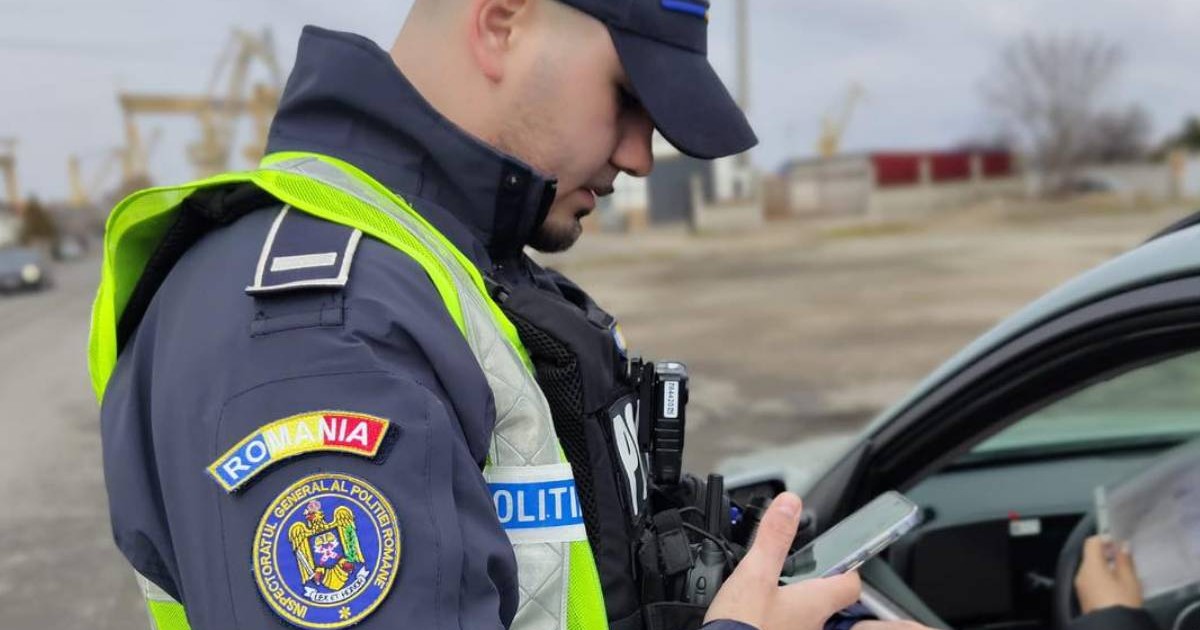 politist rutier care tine in mana actele de identitate ale unei persoane oprite in trafic, este langa o masina care are geamul deschis