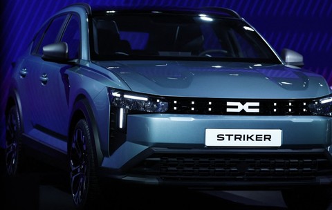 Un autoturism Dacia model Striker, de culoare gri-albăstruie, expus în cadrul unei prezentări pe un fundal iluminat în nuanțe de albastru. 