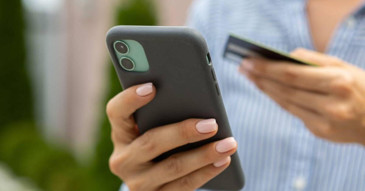 Mâini feminine țin un telefon mobil modern și un card de credit sau de debit bancar pe stradă.