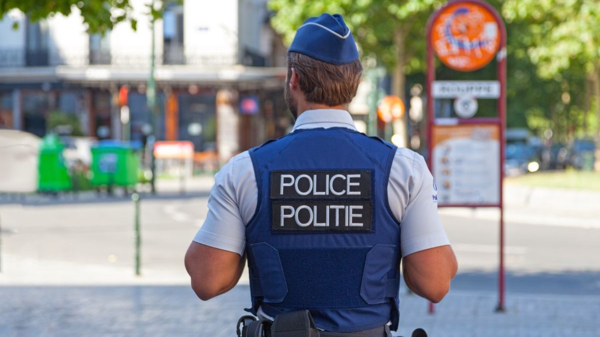 Polițist în vestă antiglonț, văzut de la spate, patrulând pe stradă, Bruxelles, Belgia